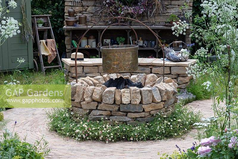 A romantic country garden with a dry-stone firepit, set into a circular path of clay setts, and separated by a collar of fleabane. The Naturecraft Garden, designed by Pollyanna Wilkinson, RHS Hampton Court Palace Garden Festival, 2019.