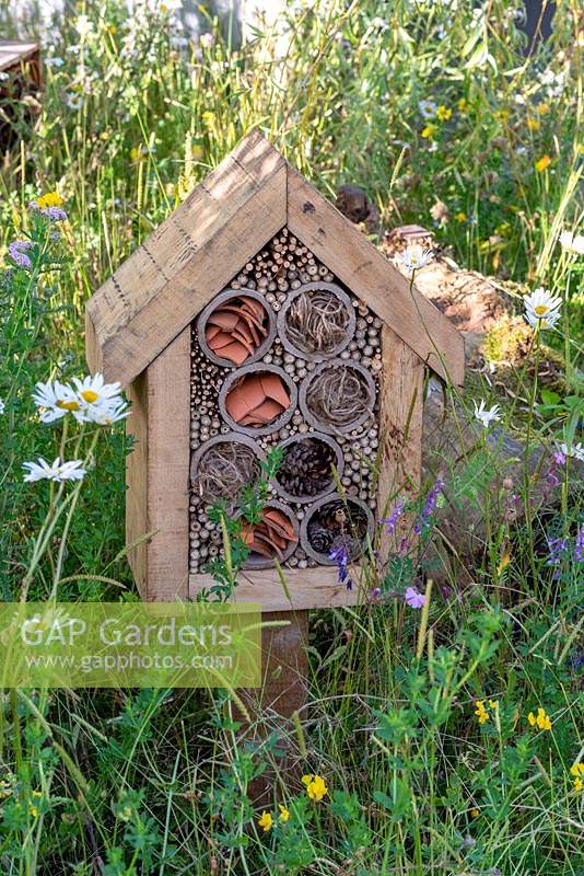 A small insect house is built in a flower meadow, in a wildlife friendly garden.