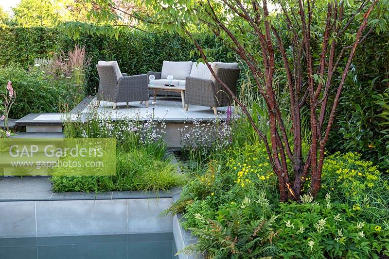 A small contemporary courtyard blends hard landscaping and a still pool with beds of wildlife friendly planting to create a calm, relaxing space. APL A Place to Meet, designed by Cherry Carmen, RHS Hampton Court Palace Garden Festival, 2019. 