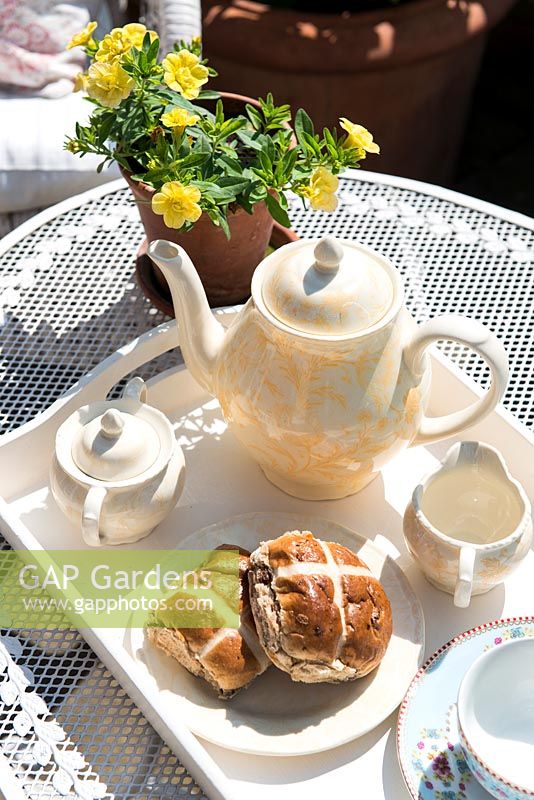 Tea pot, cups and hot cross buns on garden table 