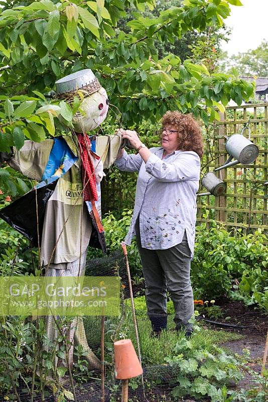 Sue Emms, tweaking a scarecrow in the contemporary cottage garden she has designed around her C18 cottage in rural Herefordshire, UK. 