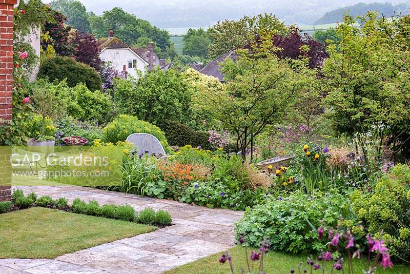 View of the South Downs, over Kingley Vale. Terrace borders of multi-stemmed amelanchiers, geums, hardy geraniums, alliums, euphorbias, Iris 'Rajah', centaureas, aquilegias and roses.