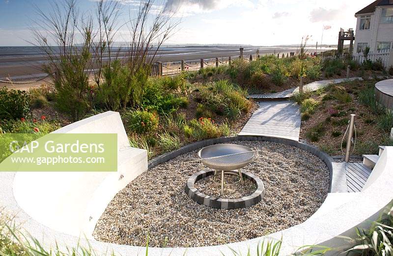 Curved seating around fire pit in sea side garden. 