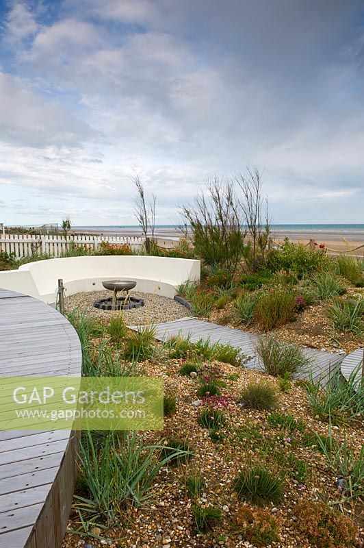 Modern, landscaped seaside garden, with curved bench and gravel borders. 