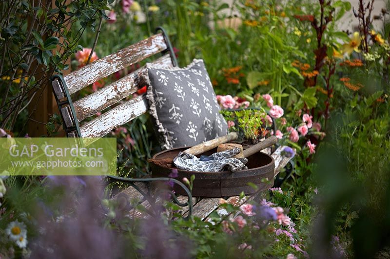 The BBC Springwatch Garden. Vintage garden seat with old tools amongst cottage-style planting. 