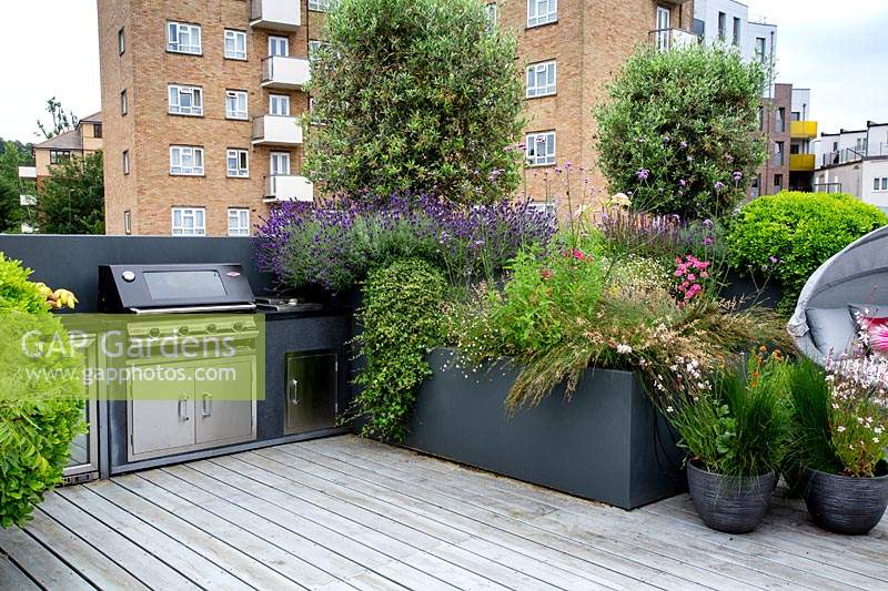 Roof terrace with wood decking, barbecue and raised beds with perennials and annuals forming a natural screen for privacy.