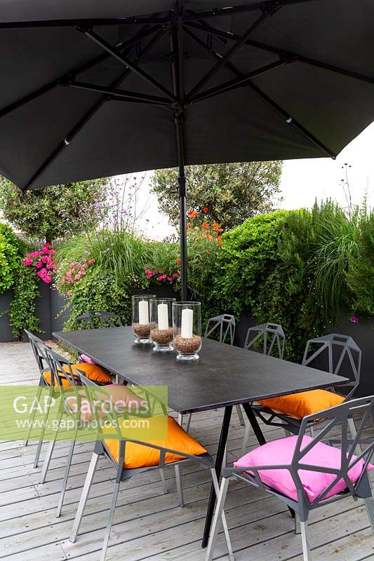 Roof terrace with wood decking and contemporary grey chairs, table and parasol. In the background raised beds with perennials and annuals forming a natural screen for privacy.