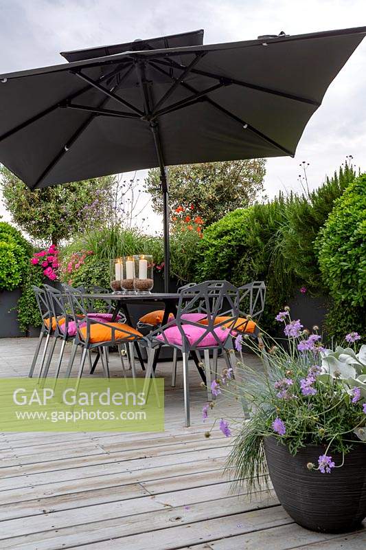 Roof terrace with wood decking and contemporary grey chairs, table and parasol. In the background raised beds with perennials and annuals forming a natural screen for privacy.