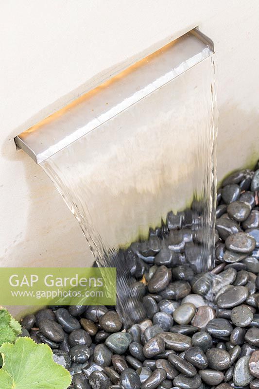 Modern water feature - simple spout from sandstone plinth onto black pebbles.