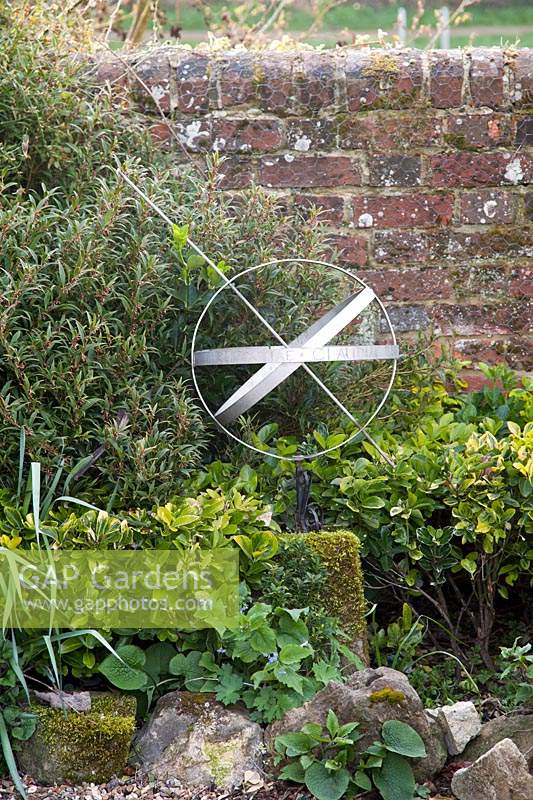 Decorative armillary sphere amongst green foliage and against a brick wall