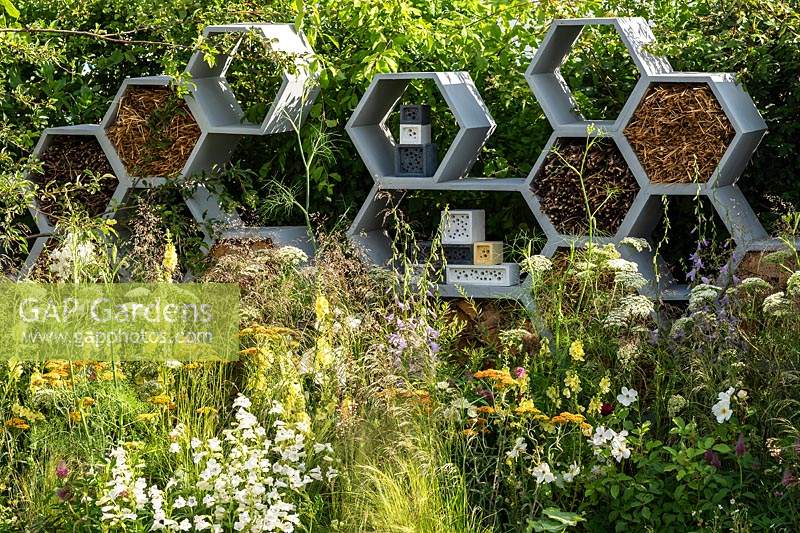 A garden planted to attract wildlife. Contemporary honeycomb shapes feature in a wall designed to be a habitat for insects, especially bees. RHS Hampton Court Palace Garden Festival 2019. Sponsor: Warner's Distillery.