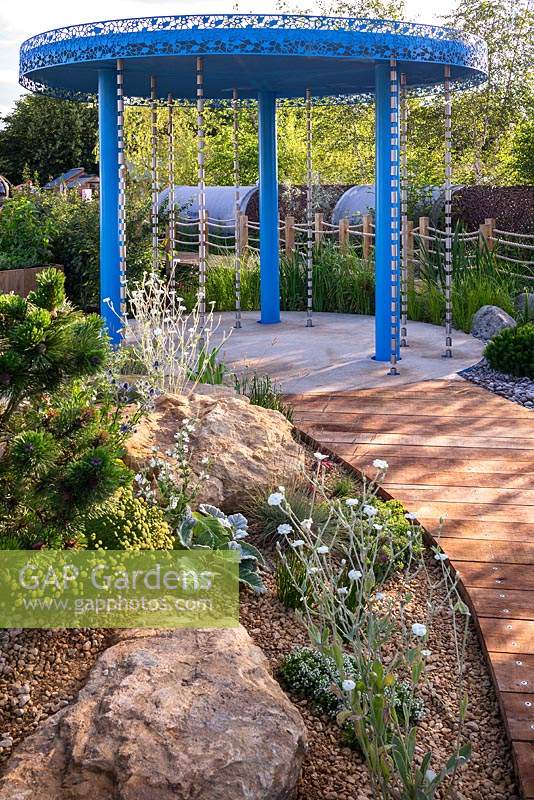 A garden designed to show how to cope with climate change. A rainfall pavilion with rain chains channels water into the garden. Large natural stones form a contemporary rock garden, with drought tolerant plants including Santolina, Lychnis coronaria 'Alba', at the RHS Hampton Court Palace Garden Festival 2019. Sponsor: Thames Water.