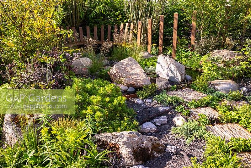 Use of natural rock and stone, with green foliage planting. RHS Hampton Court Palace Garden Festival 2019. Sponsors: Kebony, CED Stone, R and G Metal Products, William's Art  and Design, Practicality Brown.