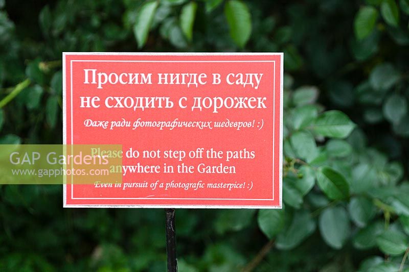 Sign reading 'Please do not step off paths anywhere in the garden. Even in pursuit of a photographic masterpiece' in The Old Apothecary's Garden - Aptekarsky Ogarod -Moscow, Russia
