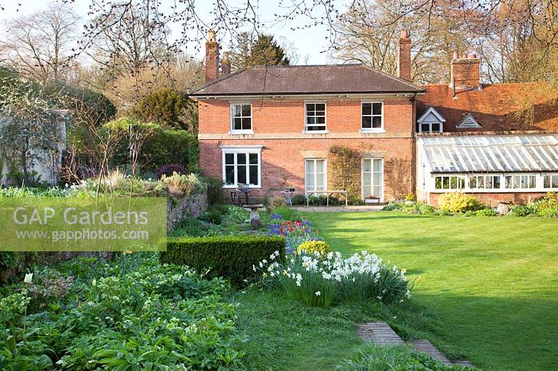 View of house across formal lawn and spring planting including clipped low hedge: Little Court, Hampshire, UK