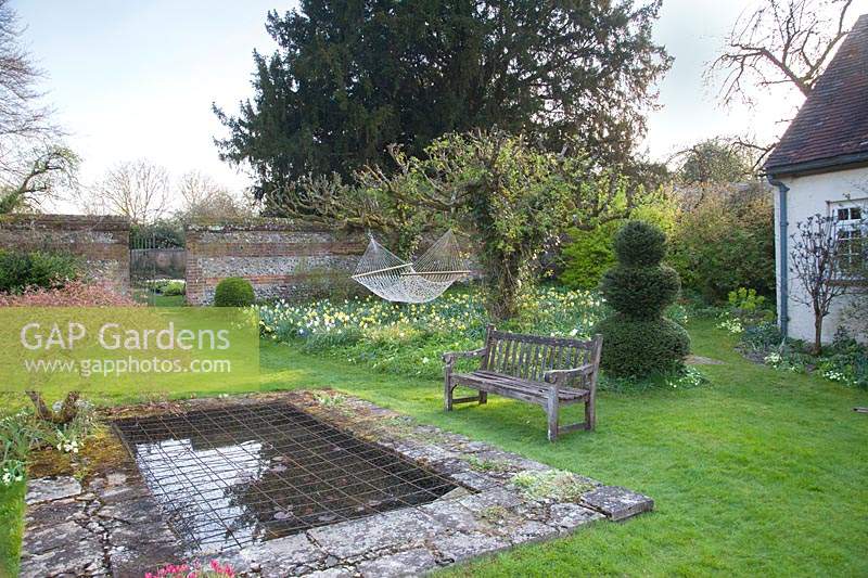 Wooden bench overlooking pond with decorative topiary and hammock:  Little Court, Hampshire, UK