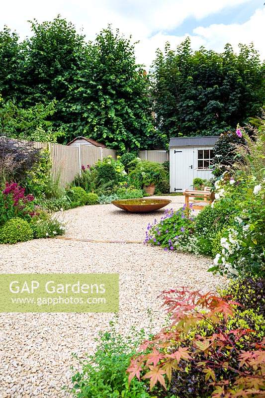 Small garden with water feature, seating area and white garden shed.