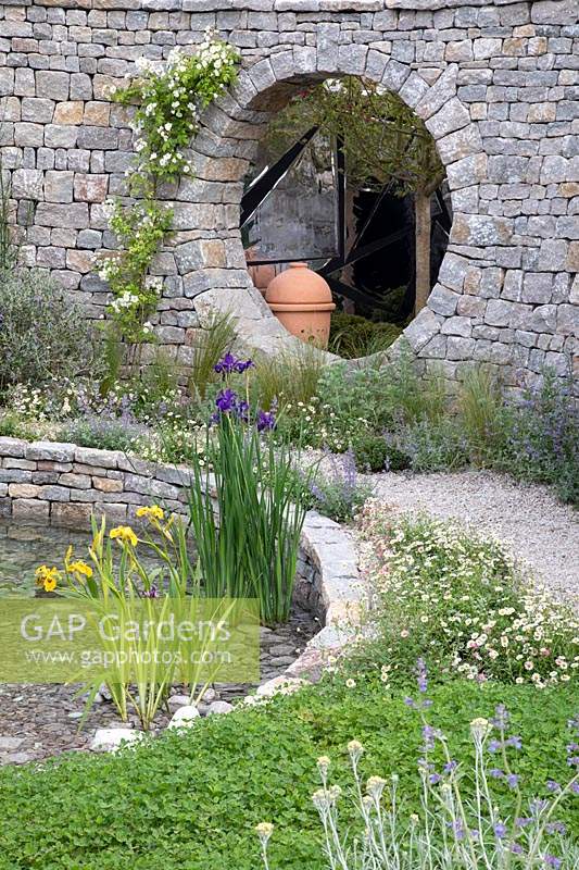 Water feature made from dry stone walling bordered by a gravel path with Stipa tenuissima bordering the pond. Garden: The Harmonious Garden of Life. Sponsor: Mr Robert and Mrs Sue Cawthorn Margheriti Piante, Italy. Chelsea Flower Show 2019.