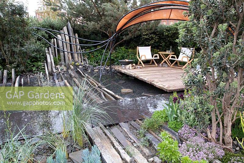 Seating area bordered by water. Garden: Facebook: Beyond The Screen. Sponsor: Facebook Gold medal. Chelsea Flower Shows 2019.
