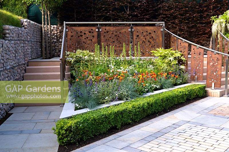 Stenciled coten steel panels under railings behind a bed of perennial planting at RHS Chelsea Flower Show 2019. Design: Marshalls