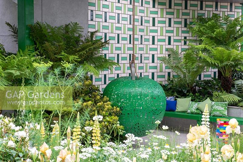 Feature Apple shape hanging seat under a tiled pavilion with Dicksonia antarctica, Lupinus 'Polar Princess', Orlaya grandiflora and Iris - The Greenfingers Charity Garden, RHS Chelsea Flower Show, 2019.
