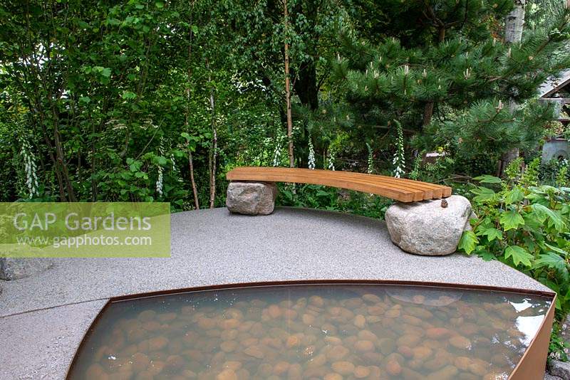 Wooden bench set on two boulders next to a pepple pool - Family Monsters Garden, RHS Chelsea Flower Show 2019
