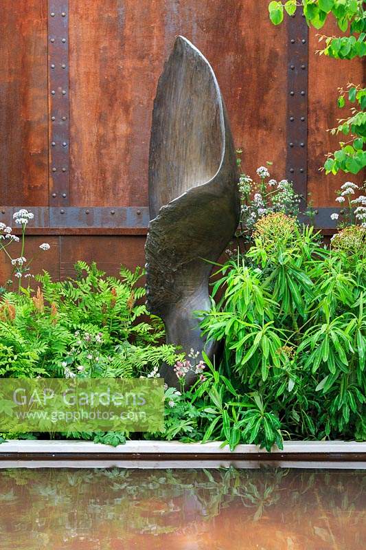 The Wedgwood Garden. Metal sculpture with water in front and wall with cladding which imitates rusted metal behind. Plants include: Osmunda regalis - Royal Fern, Astrantia major 'Alba', Ammi majus and Euphorbia pasteurii. Sponsor: Wedgwood