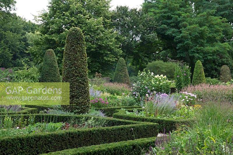 View over Buxus- Box - edged beds filled with flowers with topiary columns and trees beyond