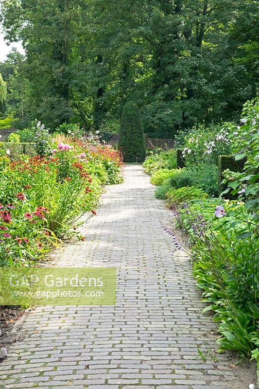 View along paved path to focal point topiary, flower border either side of path
