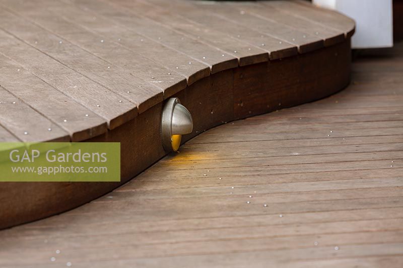 Detail of a curved hardwood timber deck showing a surface mounted stainless steel eye lid light.