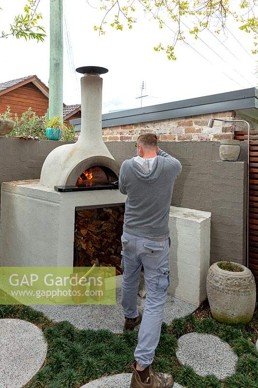 Man using a leaf blower to get the fire started in a bespoke cement rendered pizza oven.