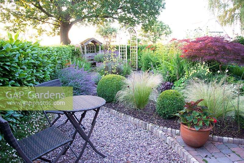 Seating area overlooking mixed borders. Early morning at 'The Homestead' an NGS garden in rural Cheshire.