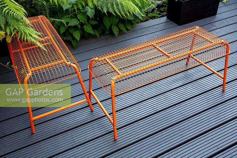 Small shade tolerant garden in London with a green theme. Dicksonia antarctica with contemporary orange seating on a grey wood deck patio.