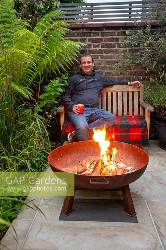 Justin Edwards sitting by a fire pit in his green oasis garden in West London.