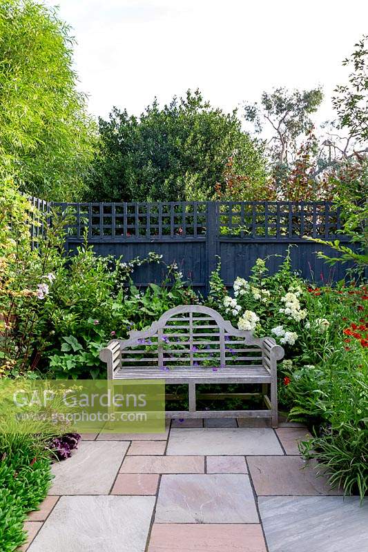 Stone patio in contemporary garden in West London with wooden seat - planting includes Helenium Moerheim Beauty, Hydrangea Vanille Fraise, Prunus Autumnalis Rosea.