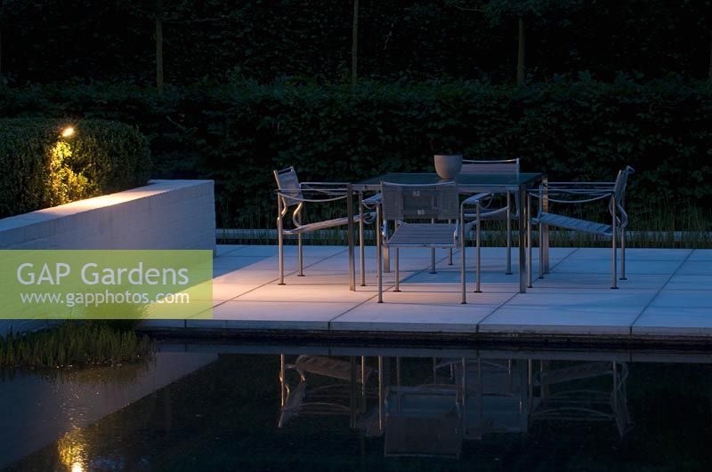 Dining area and patio surrounded by water in modern garden.