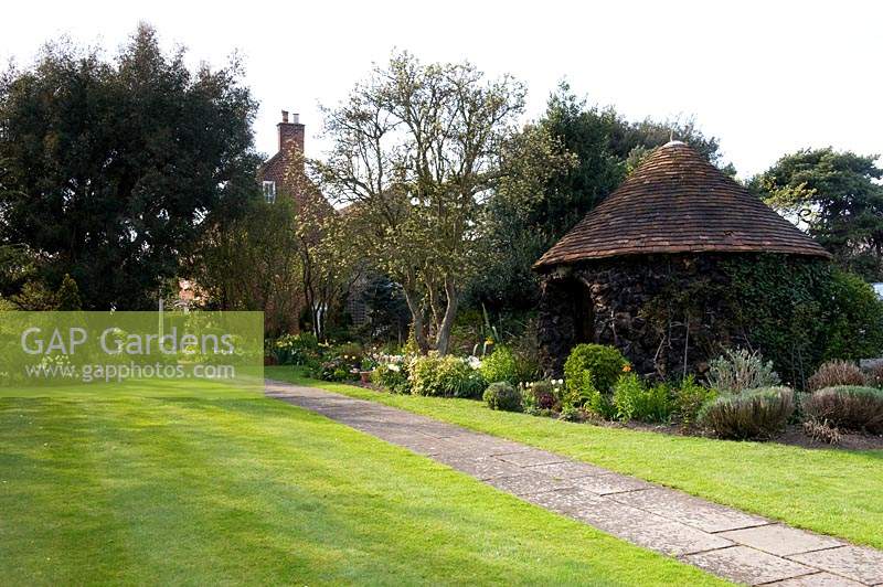 View across striped lawn to straight path and mixed border with stone outbuilding