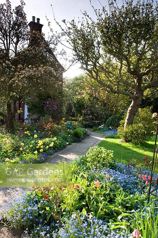 View across country-cottage style garden with borders full of flowering bulbs and perennials