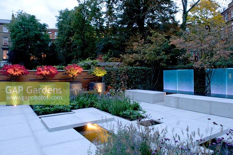View across modern city garden, with planters, illuminated by contemporary lighting at dusk 