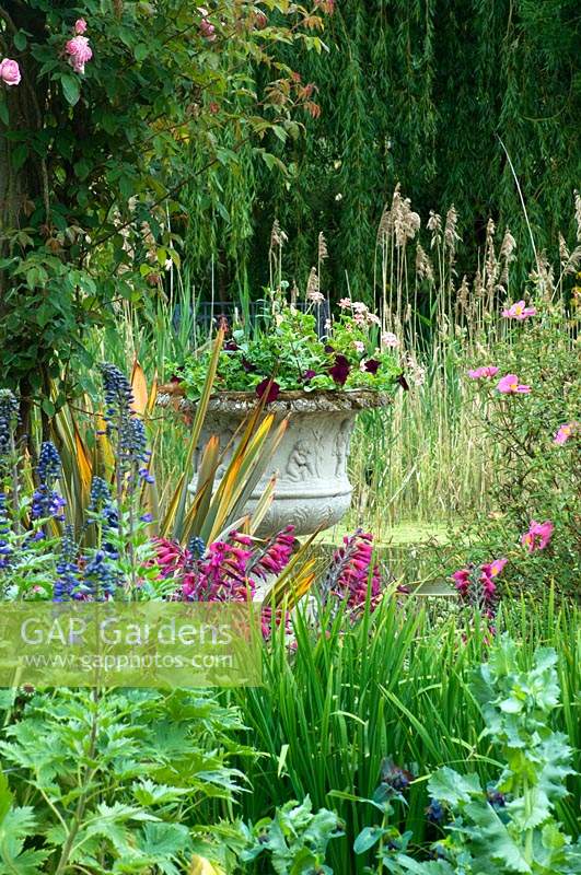 Stone urn with flowering bedding plants, surrounded by herbaceous perennials. 