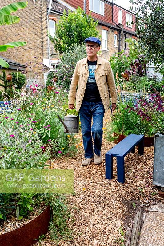 Modern cottage garden in West London. Owner and garden designer Nick Gough walking through garden with watering can.