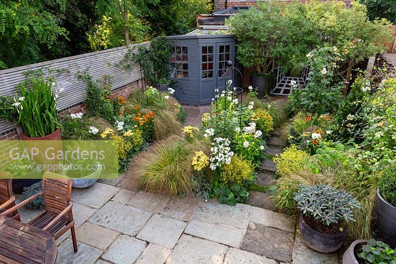 Overview of a small cottage garden with stone paved patio, mixed borders and shed. Designed by Tom Hoblyn. 