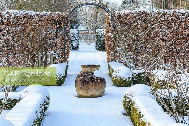 The Potager with Buxus - box hedging and topiary shapes. Fagus - Beech hedge and  terracotta oil jar with a covering of snow. The Old Rectory, Suffolk UK