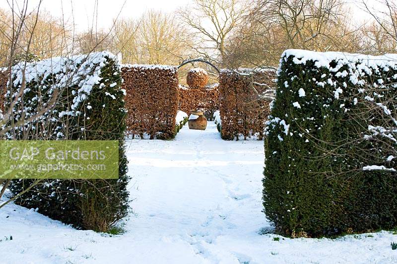 The Potager with Fagus - Beech hedges with a topiary ball and  terracotta oil jar, Taxus baccata hedges in the foreground with a covering of snow in late February. The Old Rectory, Suffolk, UK
