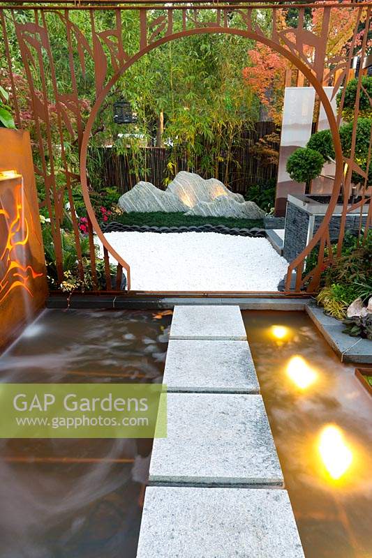 Stepping stones across a water feature through a rusty steel moongate through to a white pebble garden featuring an arrangement of stones that represent a mountain range.
