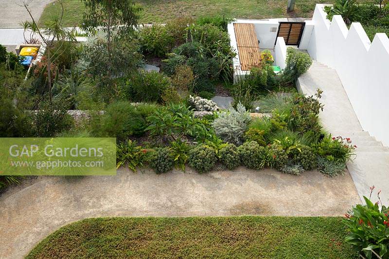 Birdseye view of a terraced garden showing a lawn, path, densely planted gardens and garbage bin bays.