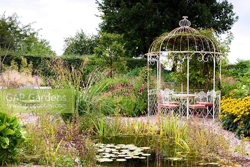 Gravel garden with naturalistic pond, metal gazebo and late season perennials and grasses in rural Nottinghamshire in September. 