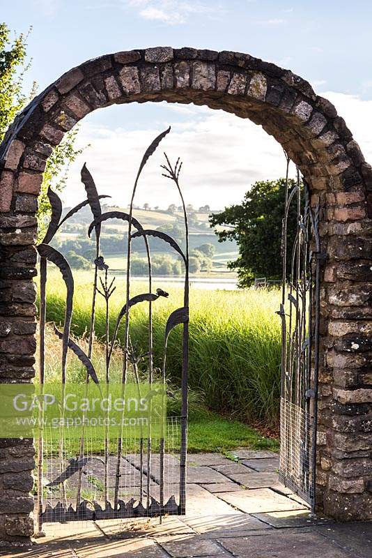 Decorative iron work gate picturing grasses and butterflies, framing a view through to Blagdon Lake 