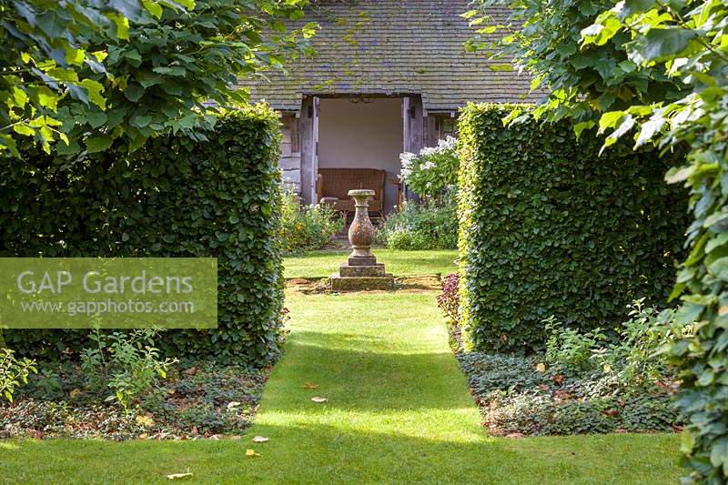 The view through the various garden rooms to the sundial in the Sundial Garden at Wollerton Old Hall Garden, near Market Drayton, Shropshire. Planting includes beech hedging and lime trees.