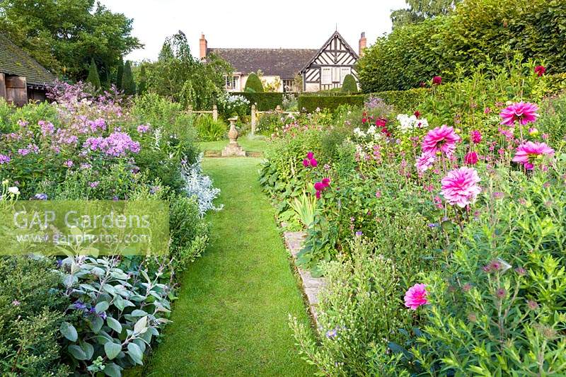 A view of the house and sundial, from the Sundial Garden at Wollerton Old Hall Garden, near Market Drayton, Shropshire. Planting includes: Phlox paniculata and Dahlias.